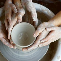 Family working on pottery wheel. Top view of mother, father and son hands making ceramic pot or sculpting clay