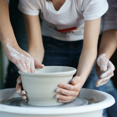 Mother teaches son to work on pottery wheel. Close up of dirty hands sculpting clay.