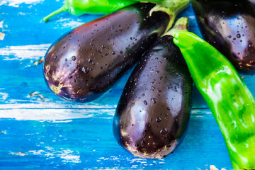 Fresh organic eggplants and green italian pepper with water drops on blue wood background, bright colors, vegetarian clean eating concept, healthy food