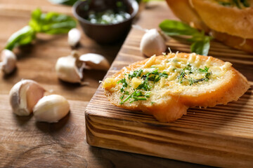 Tasty bread with garlic, cheese and herbs on wooden kitchen board, close up