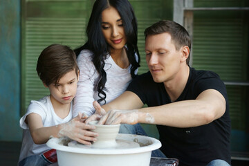 Young caucasian family working on potter's wheel. Handsome father, beautiful mother and young son. Pottery classes. Dirty Hands. Parents enjoying time together with their child.