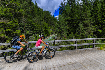 Naklejka premium Mountain biking woman and young girl along river in Dolomites, Italy
