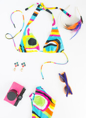 Summer background, beach outfit, girl summer stuff. Geometric abstract pattern swimsuit, pink retro camera, bright sunglasses, feather headband and earrings. Flat lay, top view.