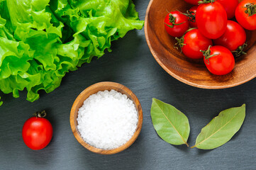 Top view: fresh cherry tomatoes, salt and bay leaves on a black background with spices