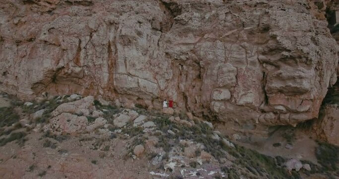 Drone footage, camera following two little girls walking on moutain path in red and white dresses