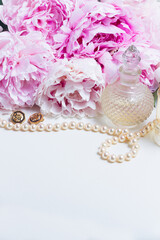 Wedding lifestyle with fresh peony flowers, glamour bottles and jewellery, copy space on white leather