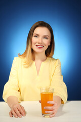 Beautiful woman sitting at table with glass of fresh juice, on color background