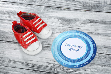Pregnancy wheel with baby booties on wooden background