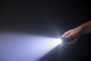 Black flashlight a beam of light directed at the viewer in male's hand isolated from right side of...