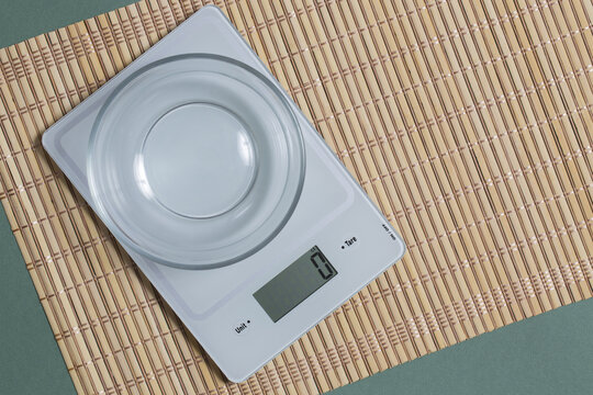 Digital Kitchen Scale With Empty Glass Bowl On Bamboo Mat And Green Paper Background.