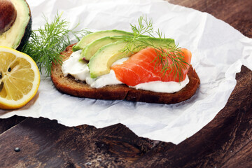 Bread with avocado and smoked salmon for lunch table. Sharing antipasti on party or summer picnic time over wooden rustic background.
