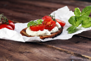Bread with cream cheese and tomato for lunch table. Sharing antipasti on party or summer picnic time over wooden rustic background.