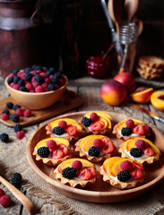 Summer dessert with various fruits. Fresh berry tartlet or cake with vanilla custard, raspberry, peach and blackberry for the whole family. Rustic style. Place for text.