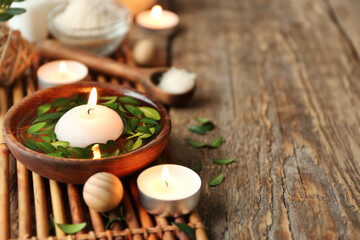 Bowl with water, green leaves and burning candle on bamboo mat
