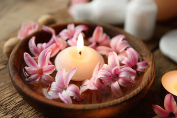 Bowl with water, hyacinth flowers and burning candle on wooden table, closeup