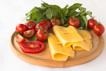 Cheese, tomato and green basil on a cutting board. White background