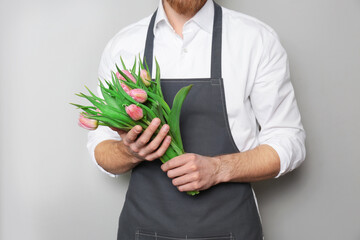 Young florist with beautiful tulips on grey background
