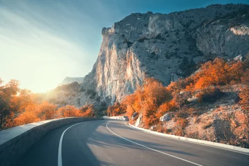 Poster Asphalt road in autumn at sunrise. Landscape with beautiful empty mountain road with a perfect asphalt, high rocks, trees and sunny sky. Vintage toning. Travel background. Highway at mountains. Nature © den-belitsky