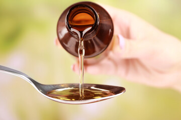 Pouring cough syrup into spoon on blurred background