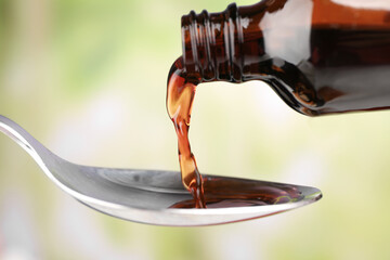 Pouring cough syrup into spoon on blurred background