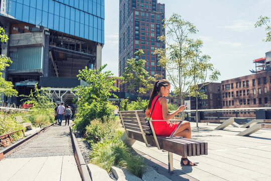 New York City Lifestyle Woman On Mobile Phone On Urban High Line Park NYC. Tourist Travel Vacation Girl Sitting On Beanch Texting On Smartphone App Visiting Manhattan Touristic Attraction.