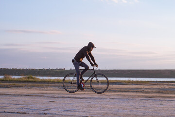 Obraz premium Alone rider on fixed gear road bike riding in the desert near river, hipster tourist bicycle rider pictures.