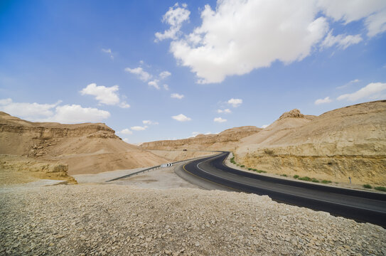 Asphalt road in the Judean desert on a background of blue sky with clouds