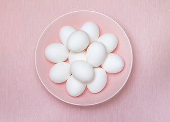 Top view of a dozen of white eggs on the pink plate and pink background, isolated. Design, visual art, minimalism, concept.