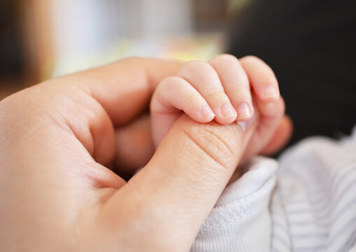Infant holding a thumb of an adult