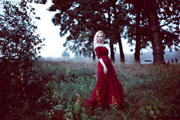 Fashion gorgeous young blonde woman in beautiful red dress in a fairy-tale forest. magic...