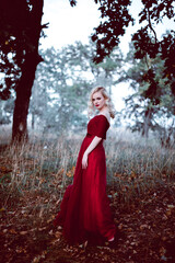 Fototapeta premium Fashion gorgeous young blonde woman in beautiful red dress in a fairy-tale forest. magic atmosphere. toning shot