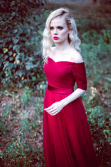 Fashion gorgeous young blonde woman in beautiful red dress in a fairy-tale forest. magic atmosphere. toning shot