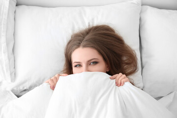 Beautiful woman hiding face under blanket in bed
