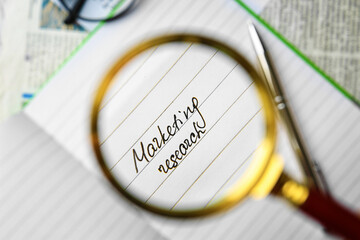 Open notebook with text MARKETING RESEARCH through magnifier, closeup