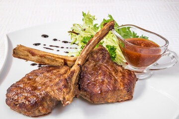 Delicious barbecue. Appetizing pieces of roasted meat on bones, herbs and sauce, on a white plate. Horizontal frame