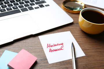 Paper sheet with text MARKETING RESEARCH and laptop on table