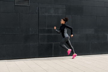 Fototapeta na wymiar Side view of female athlete running near a wall