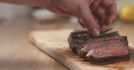 man decorating sliced medium rib eye steak with rosemary branch, wide photo