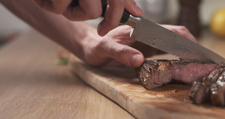 man slicing cooked medium rib eye steak on board, wide photo