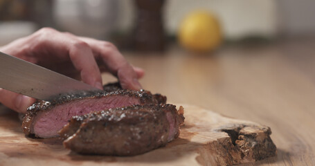man slicing cooked medium rib eye steak on board, wide photo