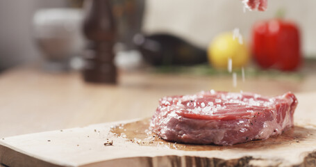 salt falling on raw rib eye steak on board, wide photo