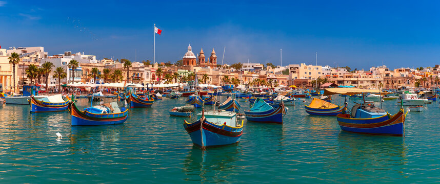 Fototapeta Panorama with raditional eyed colorful boats Luzzu in the Harbor of Mediterranean fishing village Marsaxlokk, Malta