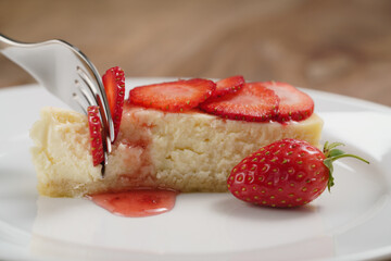 cheesecake with strawberry on plate closeup eaten with fork, shallow focus