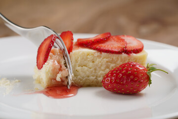 cheesecake with strawberry on plate closeup eaten with fork, shallow focus