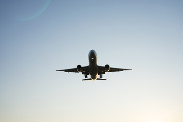 Silhouette of airplane sitting down above fields on sunrise in blue clear sky close to aeroport.