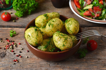 Young, boiled potatoes with butter and dill on a wooden background.