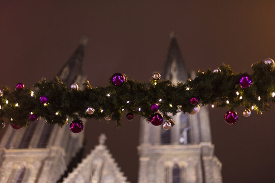 Decorative christmas ornaments (baubles) on green evergreen girlands  at the outdoor christmas markets in Prague, Czech republic, with the church of Saint Ludmila in the background