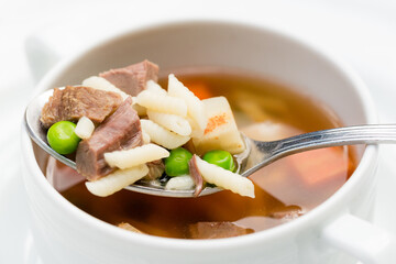 A bowl of delicious beef and barley soup with carrots, tomato, potato, celery, and peas.