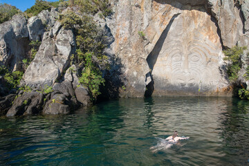 Tourist swimming in Great Lake Taupo with Maori rock carvings the iconic tourist attraction place in Lake Taupo, New Zealand.