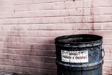 An old beaten rusty blue trash can standing in front of an old pink brick wall with a czech writing saying 